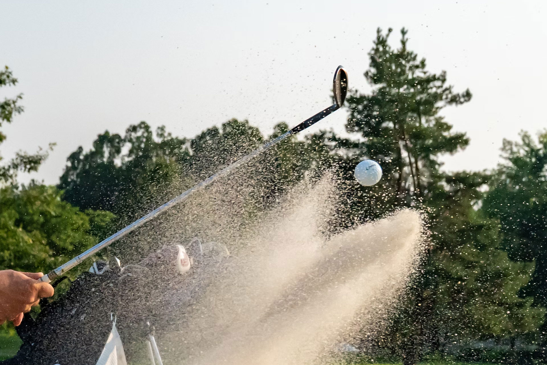 Someone hitting a golf ball from a sand bunker