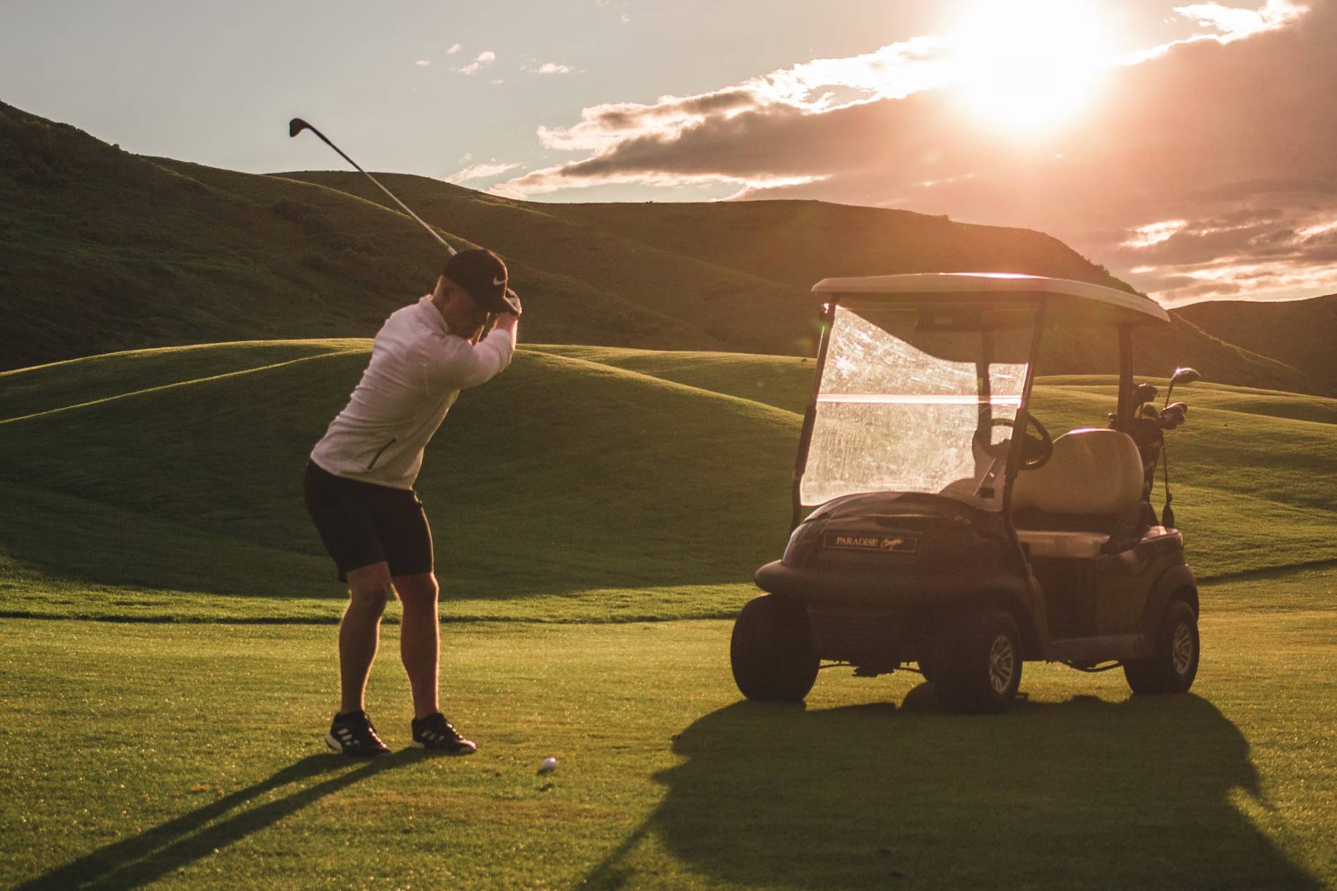 A man taking a golf shot next to a golf cart