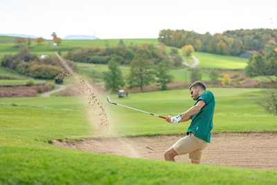 A man gitting a golf ball our of a sand bunker